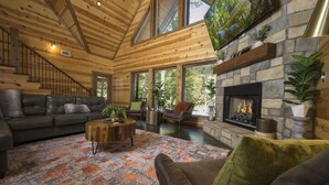 Un salon spacieux avec une cheminée en pierre, des canapés en cuir et une grande fenêtre donnant sur une forêt.