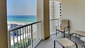 A balcony with a view of the ocean and a cityscape. There is a table and two chairs.