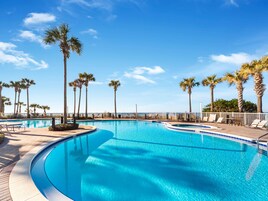 A clear blue swimming pool with palm trees and lounge chairs around it.