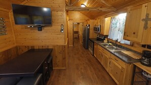 Een houten hut van binnen met een keuken, een eethoek en een aan de muur bevestigde televisie.