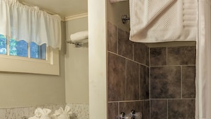 A bathroom with a toilet, a shower with a tiled wall, and a window with curtains. - Rustic Traditional Cabin_Cabin 10B (Bar Harbor)