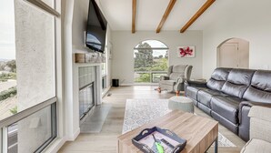 A spacious living room with a fireplace, leather sofa, and large windows offering a view of the outdoors. - San Marcos Getaway w/ Deck & Lake Views! (San Marcos)