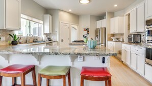 A spacious kitchen with granite countertops, white cabinetry, and stainless steel appliances. There are three wooden bar stools with red cushions. - San Marcos Getaway w/ Deck & Lake Views! (San Marcos)