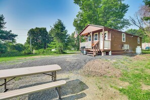 Une cabane en bois avec un porche, une table de pique-nique et un petit espace extérieur équipé d’un barbecue.