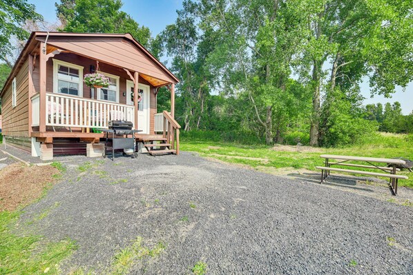 Une cabane en bois avec une véranda, un barbecue et une table de pique-nique.