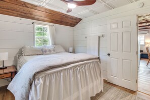 Une chambre à coucher avec un lit, une table de chevet, une fenêtre avec des rideaux, un plafond en bois et une porte blanche.