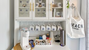 Eine Küche mit einer Kaffeestation, einem Schrank mit dekorativen Tassen und einer aufhängbaren Tragetasche.
