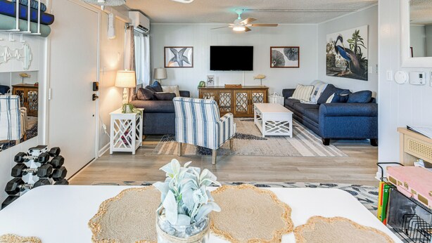 Ein Wohnzimmer mit einer Couch, Sesseln, einem Couchtisch, einem Fernseher und einem Deckenventilator.