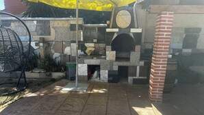 Un espace cuisine extérieur doté d’un plan de travail en pierre, d’un four en briques et d’un parasol jaune offrant de l’ombre.