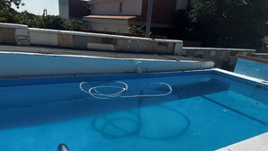Une piscine aux eaux d’un bleu limpide, avec un tuyau apparent et une rampe métallique.
