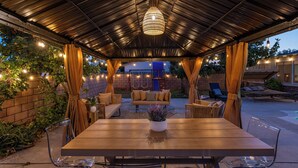 Una veranda esterna con tavolo e sedie in legno, una lampada a sospensione e un muro in mattoni con piante.