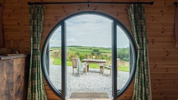 Een houten kamer met een groot rond raam, een houten tafel en twee stoelen.