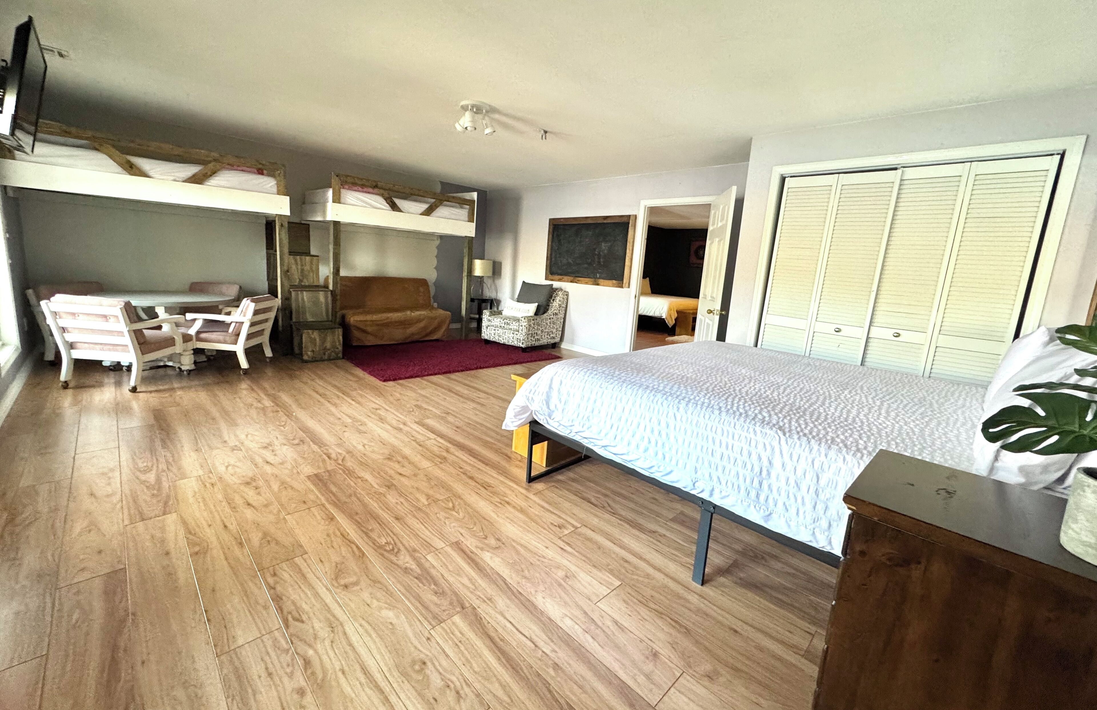 Une chambre avec un lit superposé, un bureau avec des chaises, une table de chevet et une grande fenêtre.