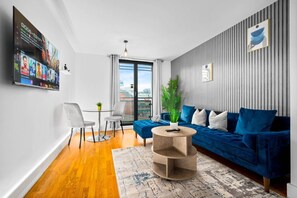 Un salon moderne avec un canapé bleu, une table basse ronde et un téléviseur à écran plat fixé au mur.