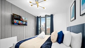 Et moderne hotelværelse med en stor seng, et fladskærms-tv monteret på væggen, udsigt over byen gennem vinduet og en moderne lampe.
