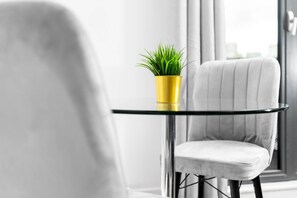 A modern room with a round glass table, a yellow pot with green plants, and a white upholstered chair.