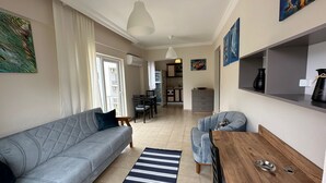 A modern living room with a grey sofa, a wooden coffee table, and a blue armchair. There is a dining area with a table and chairs, and a kitchen in the background. - Kemer Comfort Apartment (Kemer)