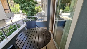 A balcony with a round table and a chair, a metal railing, and a view of greenery and buildings. - Kemer Comfort Apartment (Kemer)
