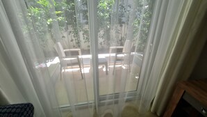 A room with a large window covered by sheer curtains, revealing an outdoor seating area with two tables and chairs. - Kemer Comfort Apartment (Kemer)