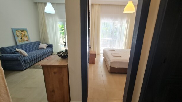 A room with a blue sofa, a wooden table, a bed with white bedding, and a window with curtains. - Kemer Comfort Apartment (Kemer)