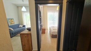 A narrow hallway leading to a bedroom with a bed, a bedside table, and a window. - Kemer Comfort Apartment (Kemer)