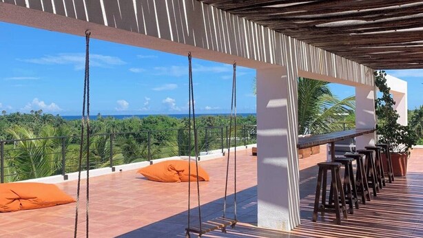 Un espacio al aire libre cubierto con terraza, sillas colgantes y una zona de bar con taburetes.