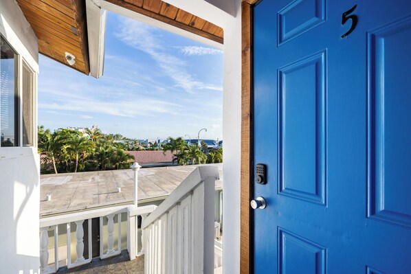 A blue door with the number 5, a white railing, and a view of palm trees and buildings in the background.