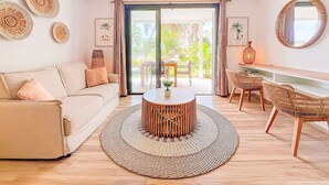 A modern living room with a sofa, a round coffee table, wicker chairs, and a large window with a view of greenery. - Casa Amour, cosy studio en bord de mer (Orient Bay)