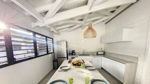 A modern kitchen with a large island, white cabinetry, and a hanging light fixture. - Marina Beach – 2 Adjacent Apartments, Marina View, Walkable Beach (Anse Marcel)
