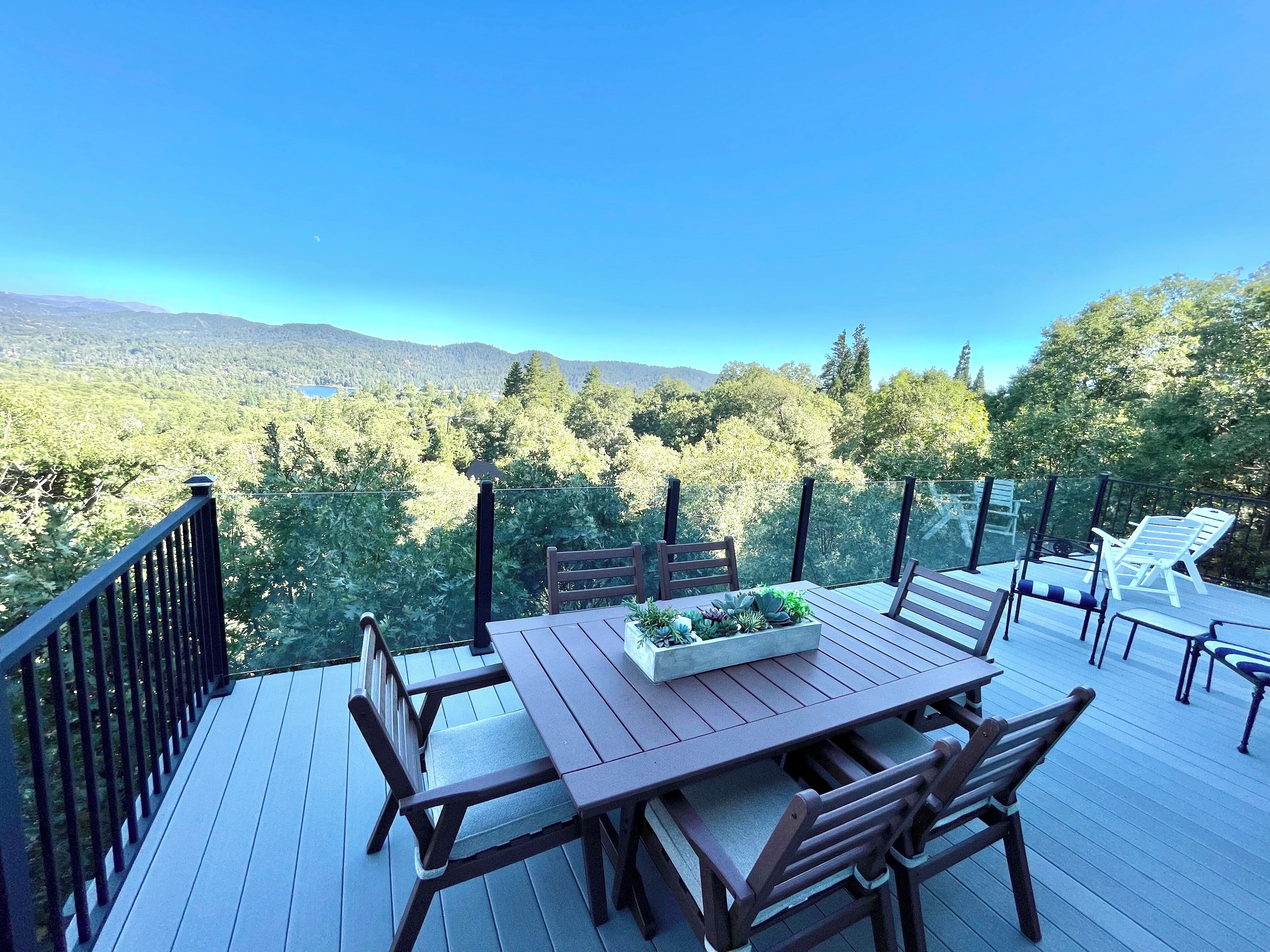 A wooden deck with a table and chairs, a planter box with plants, and a view of a forested valley.
