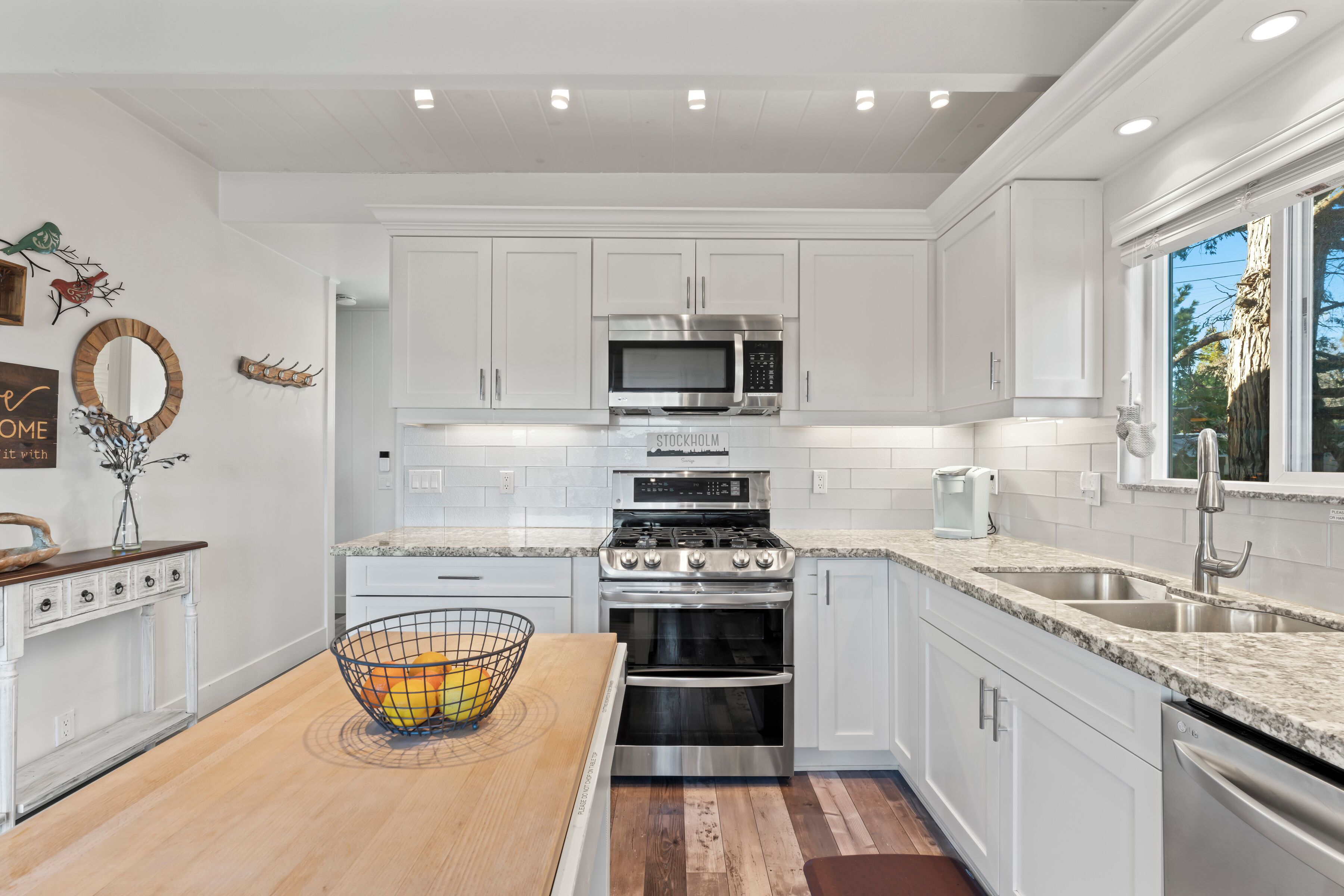 Una cocina moderna con armarios blancos, electrodomésticos de acero inoxidable, encimera de granito y una mesa de comedor de madera.
