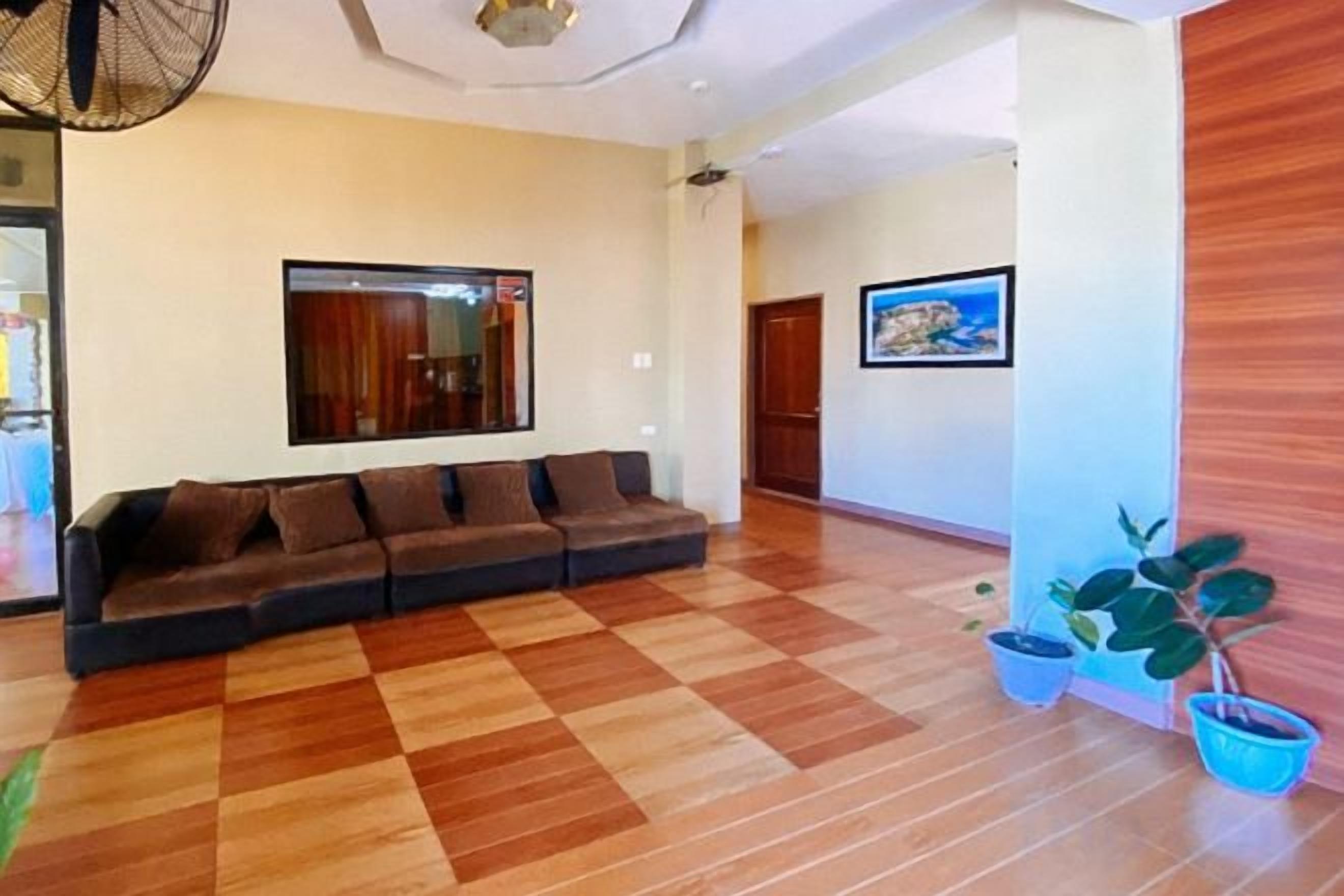 Sala de estar com sofá, piso de madeira, TV fixada na parede e duas plantas em vasos.