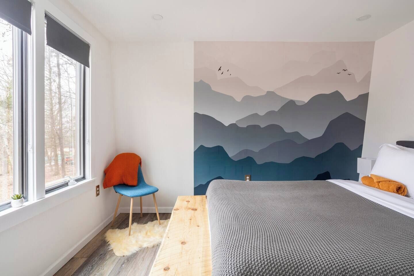Un dormitori amb llit, una cadira, una finestra gran i un mural a la paret.
