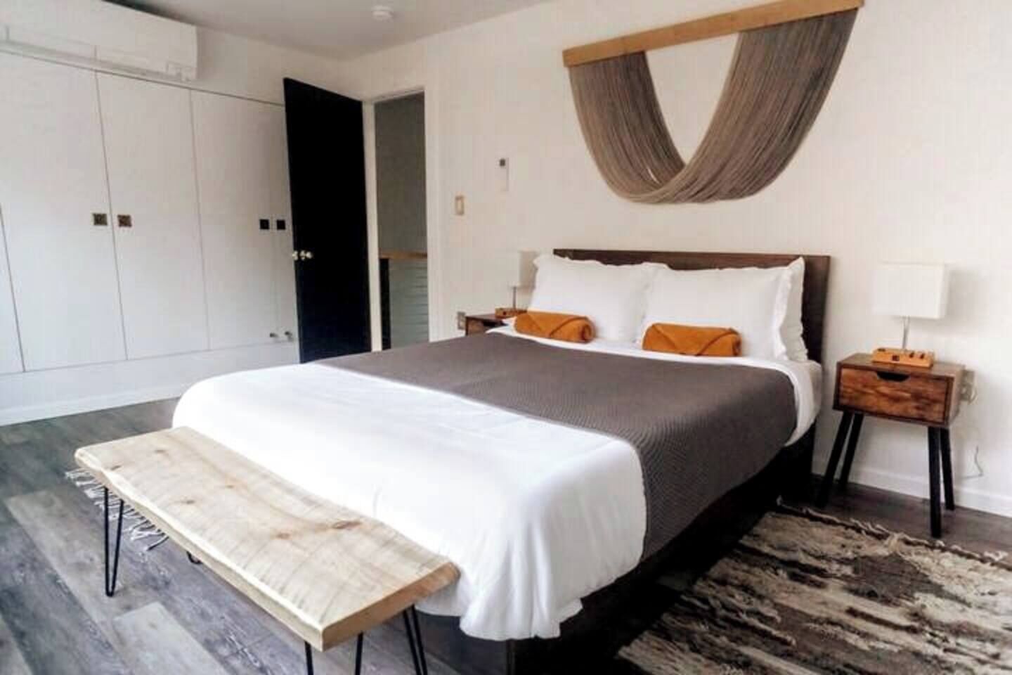 A modern bedroom with a large bed, a bench at the foot of the bed, a wooden nightstand, and a large wardrobe.