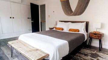 A modern bedroom with a large bed, a bench at the foot of the bed, a wooden nightstand, and a large wardrobe.