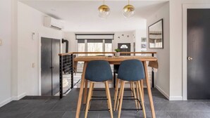 Une cuisine moderne avec un coin repas, comprenant une table en bois, deux chaises et des luminaires suspendus.