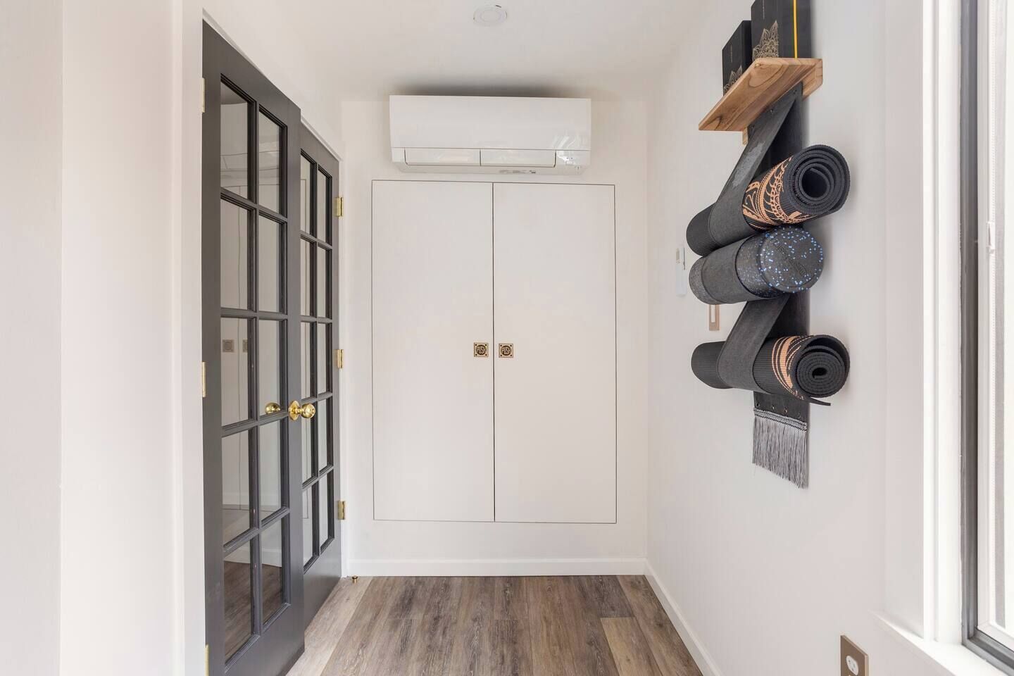 Een gang met een houten vloer, een witte deur met gouden handvat en een luchtverwarmingsunit aan de muur.