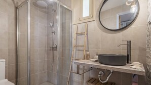 Ein Badezimmer mit einer gläsernen Duschkabine, einer Holzleiter, einem runden Spiegel und einem Waschbecken mit Aufsatzbecken.