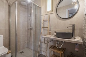 A bathroom with a glass-enclosed shower, a wooden ladder, a round mirror, and a sink with a vessel basin. - Hilani House by Homie (São Vicente)