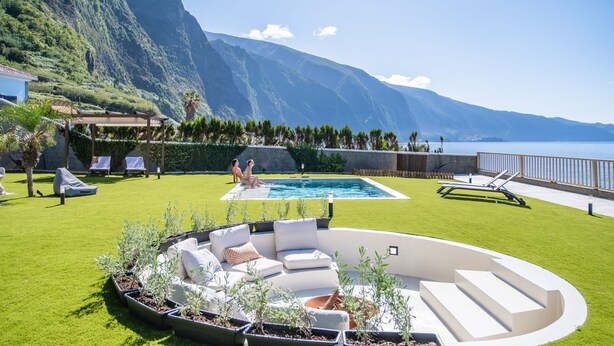 Ein Poolbereich mit einer geschwungenen Sitzgruppe, Blick auf das Meer und einer Bergkulisse.