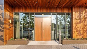 A modern building entrance with a wooden facade, glass doors, and a number '48' above the entrance. - Rainey St 1BR | Heated Pool | Gym | Bar | DT ATX (Austin)