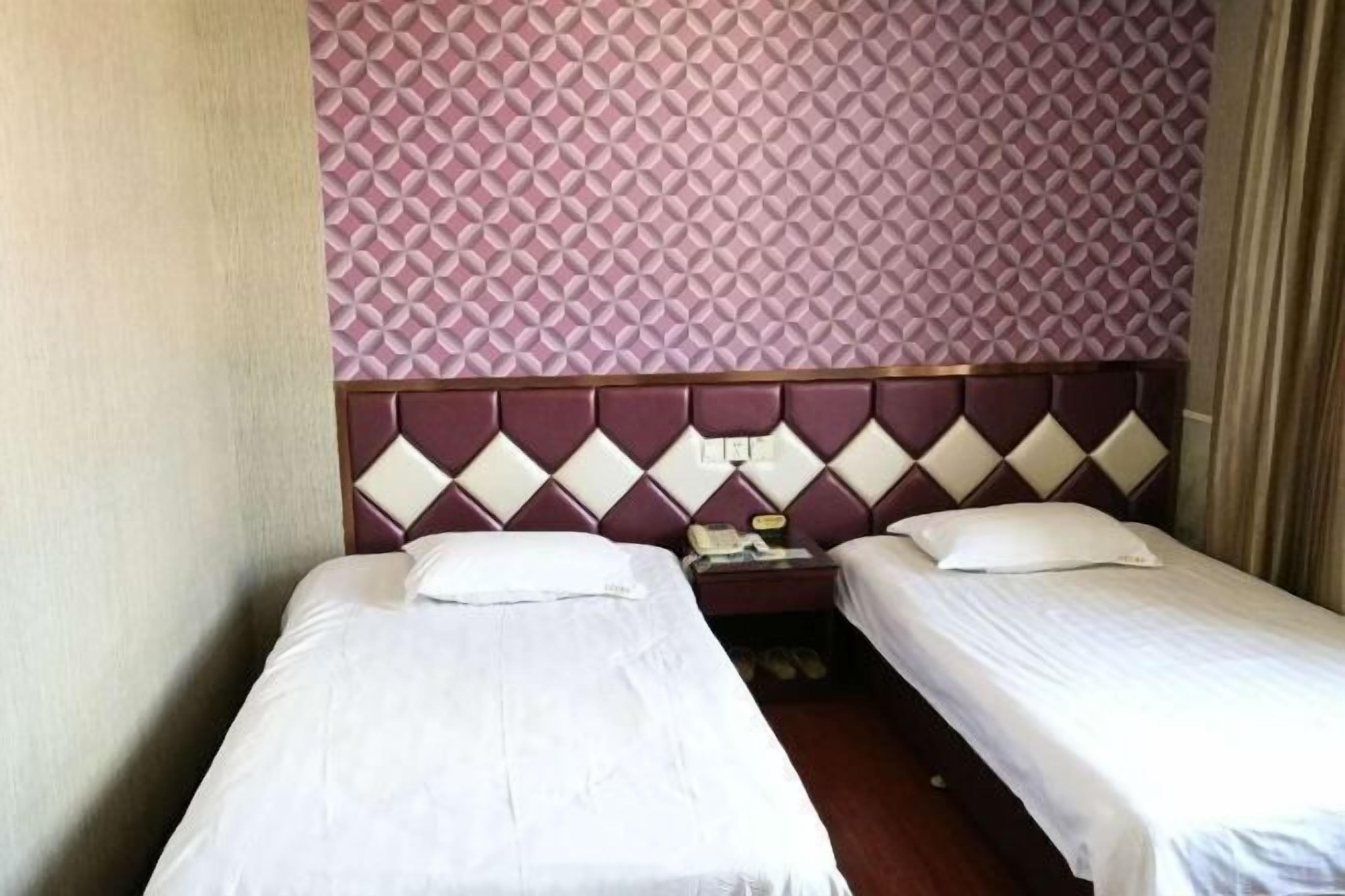 A hotel room with two single beds, a headboard with a diamond pattern, a telephone, and a pair of shoes on the floor.