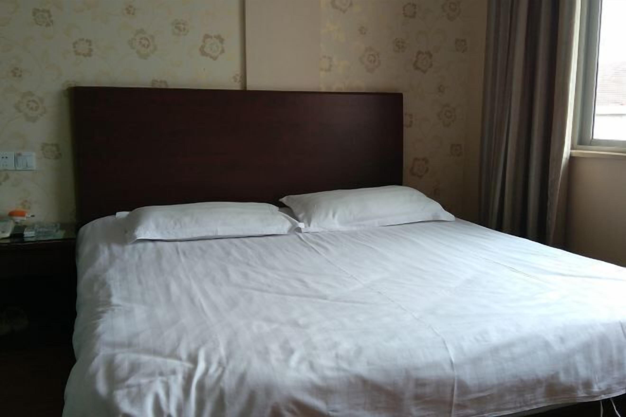 A neatly made bed with white linens, a wooden headboard, and a patterned wallpaper background.