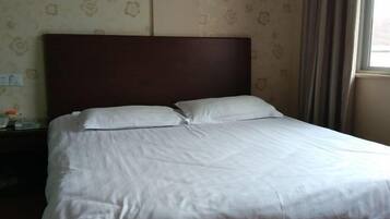 A neatly made bed with white linens, a wooden headboard, and a patterned wallpaper background.
