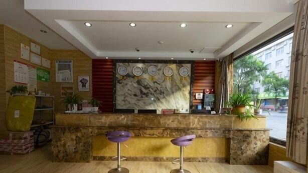 A reception area with a marble counter, two purple bar stools, a large window with a view of the street, and a wall with informational posters. - Hengdian Jinwo Hotel (Dongyang)