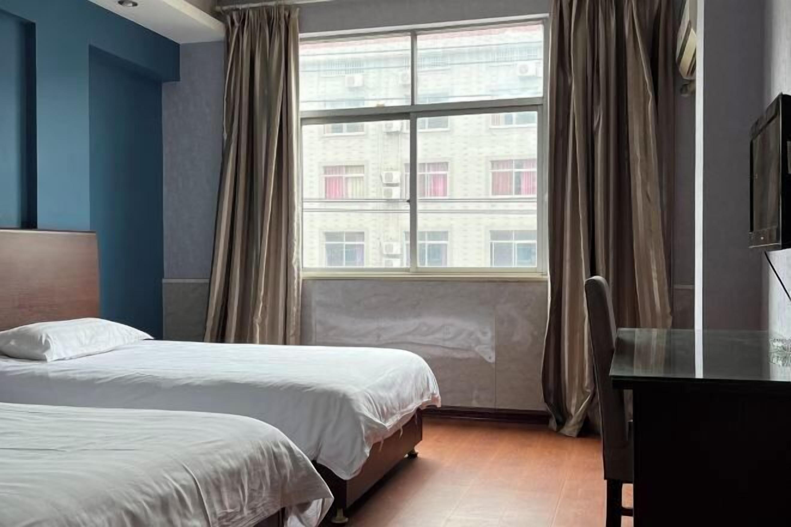 A hotel room with two beds, a desk, a chair, and a large window with curtains.