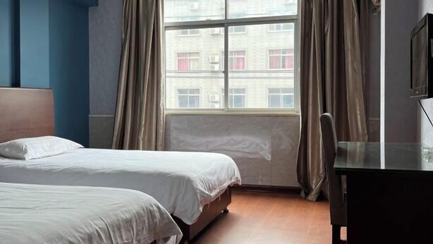 Una habitación de hotel con dos camas, un escritorio, una silla y un amplio ventanal con cortinas.