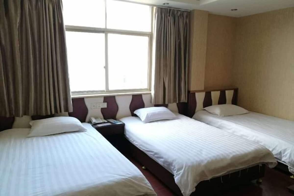 A hotel room with two single beds, a nightstand, a window with curtains, and a wall-mounted telephone.