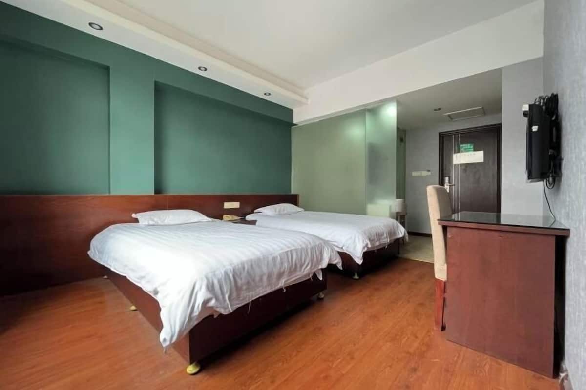 A hotel room with two beds, a wooden desk, a TV, and a door with a sign.