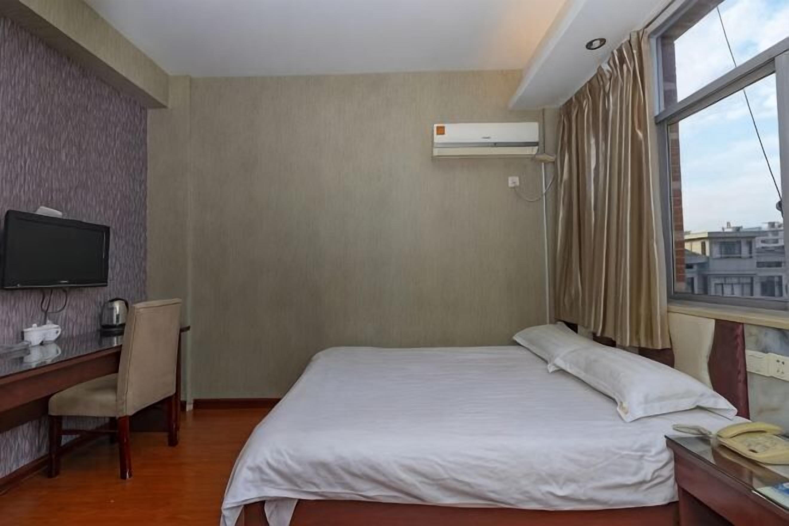 Una habitación de hotel con cama, escritorio, silla, televisor y ventana con cortinas.